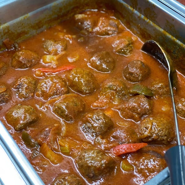 Ana Restaurant's meatballs in a rich red sauce with peppers and onions, served in a metal tray.