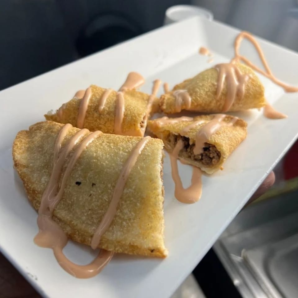 Four golden-brown empanadas, one cut open to show a savory filling, drizzled with a creamy sauce.