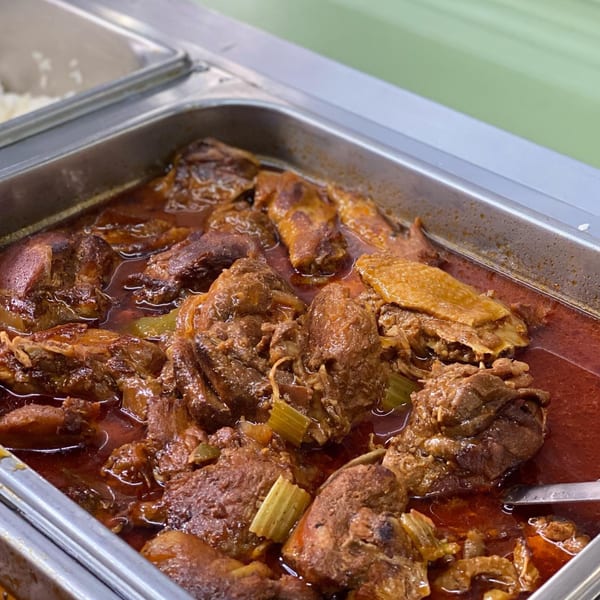 Close-up of Ana Restaurant's braised meat and vegetables in a rich red sauce, served in a metal buffet tray.