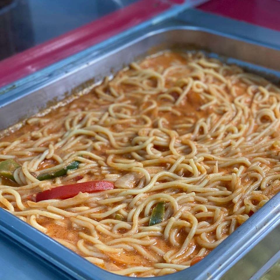 Close-up of creamy noodles with red and green peppers in a metal serving dish at Ana Restaurant.