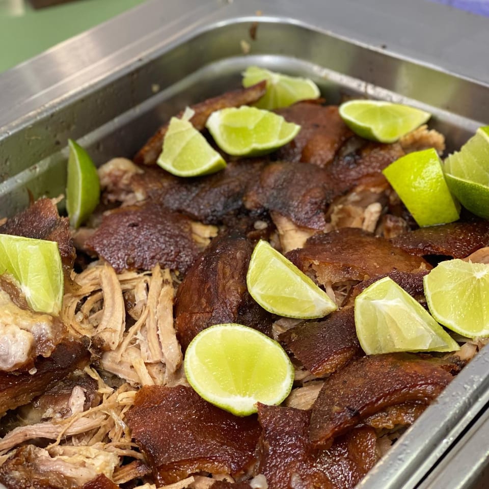 Crispy roasted pork with shredded meat and lime wedges in a metal serving tray.